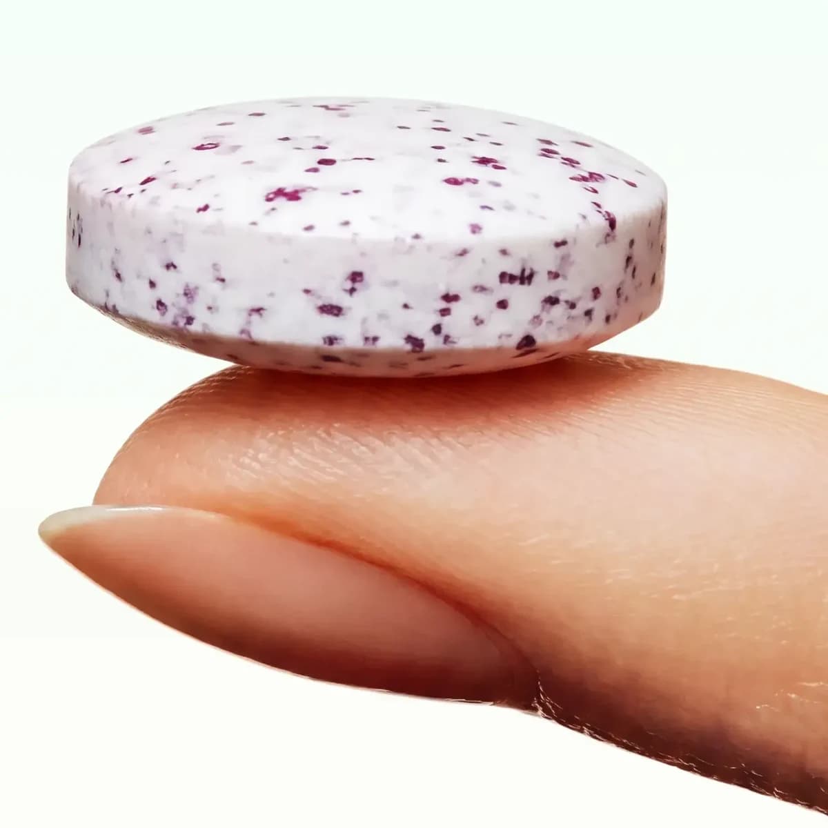A Viome oral lozenge on a fingertip, about the size of a mint